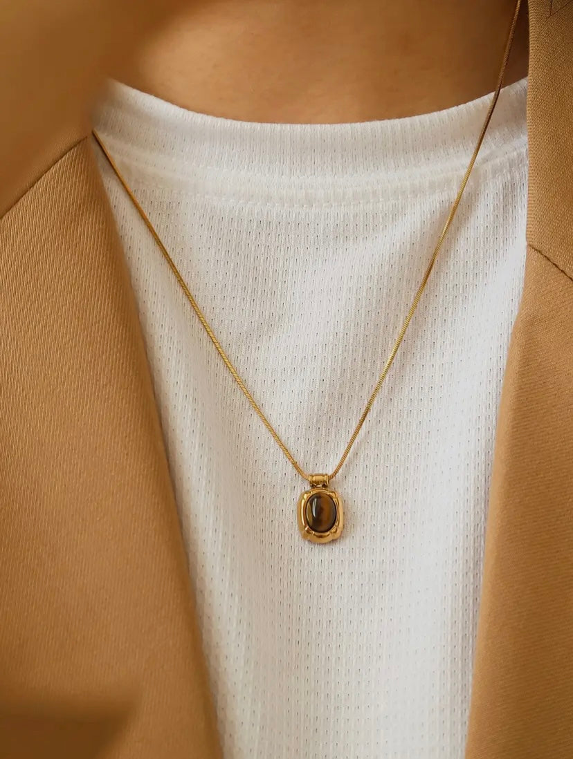 18 ct Gold necklace with a pendant on a person wearing a white top and beige jacket.