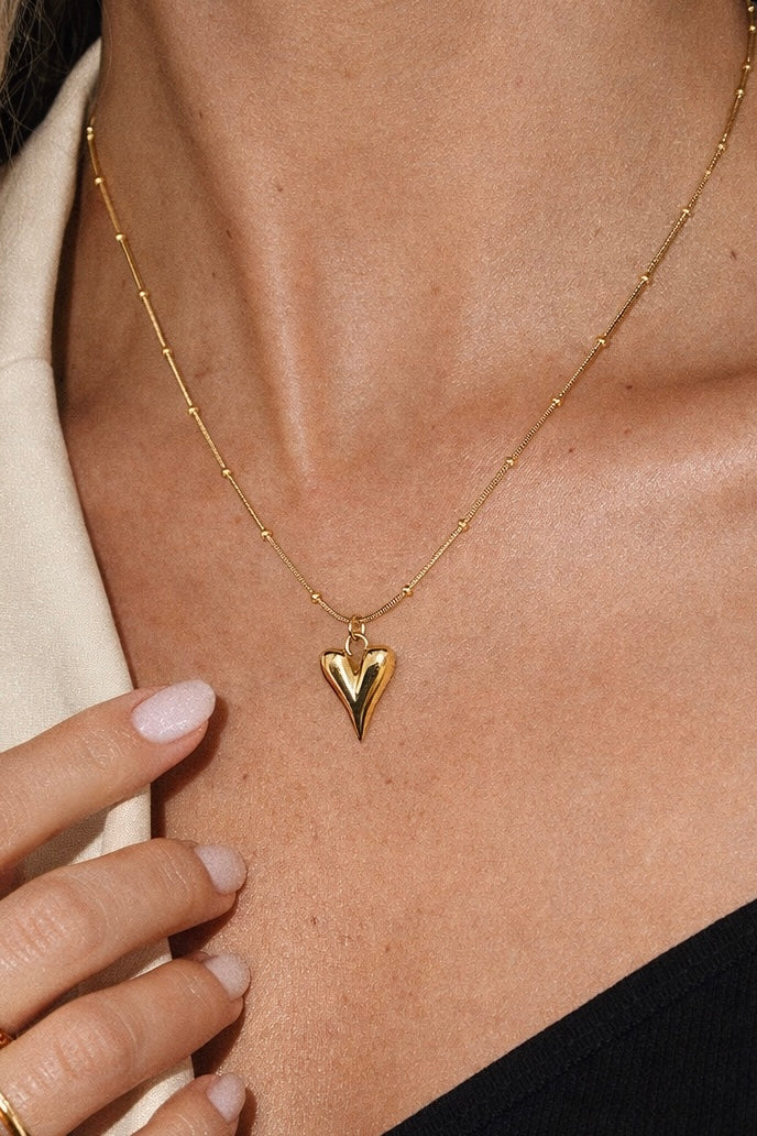 Gold necklace with a heart pendant worn by a person
