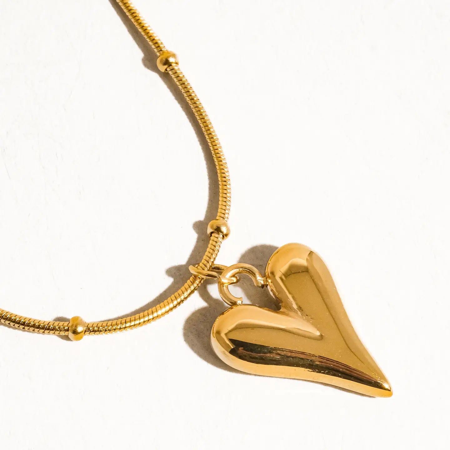 Gold necklace with a heart-shaped pendant on a white background