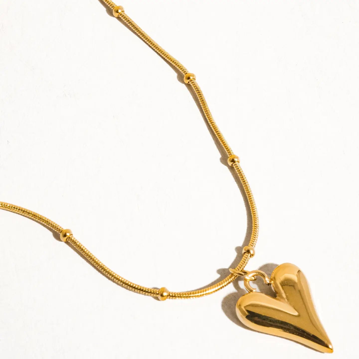 Gold necklace with a heart-shaped pendant on a white background