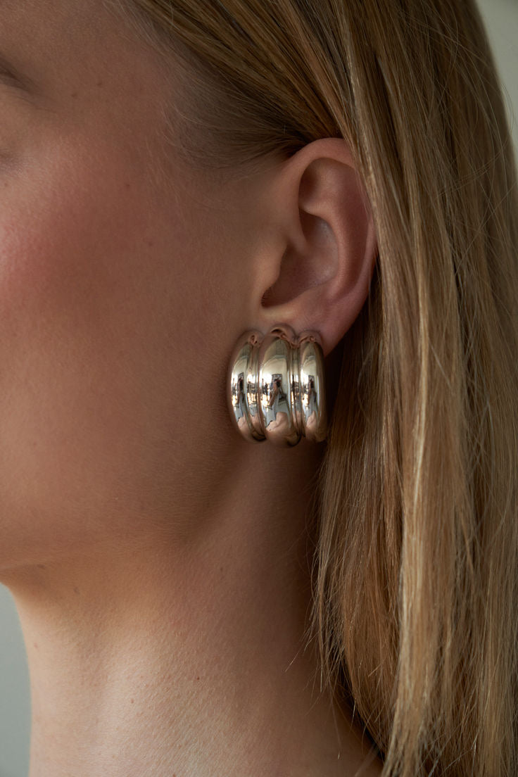 Close-up of a person wearing a stainless silver hoop earring with a neutral background