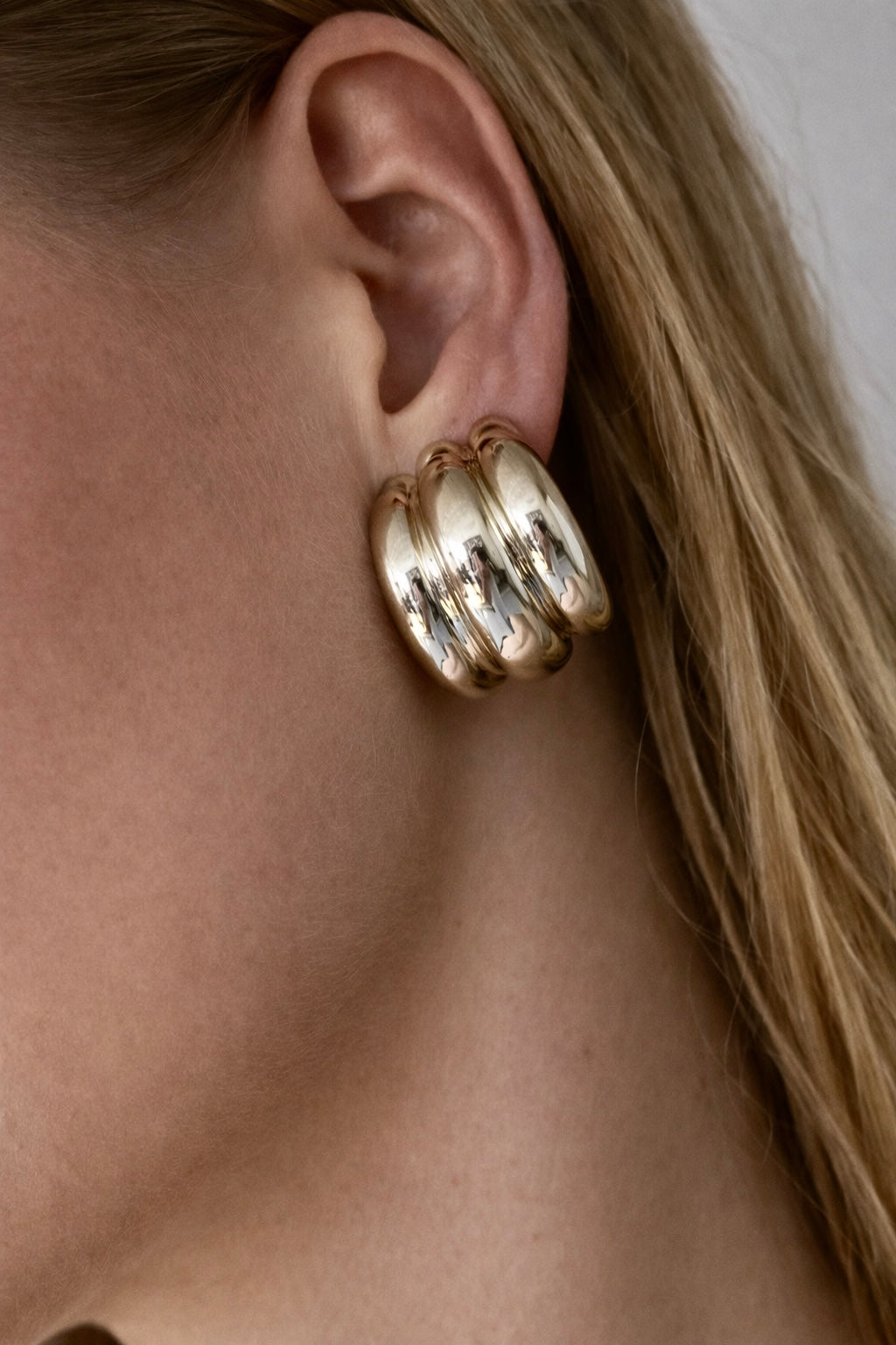 Close-up of a person wearing a gold hoop earring with a neutral background